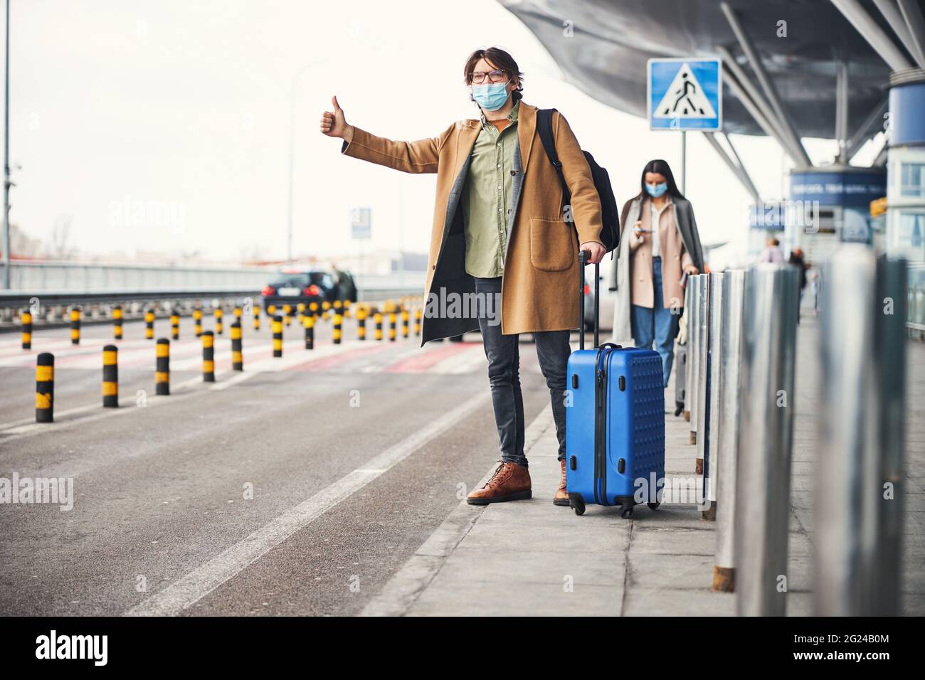 Stilvoller junger Mann in medizinischer Maske, der am Flughafen ein Taxi nimmt Stockfoto