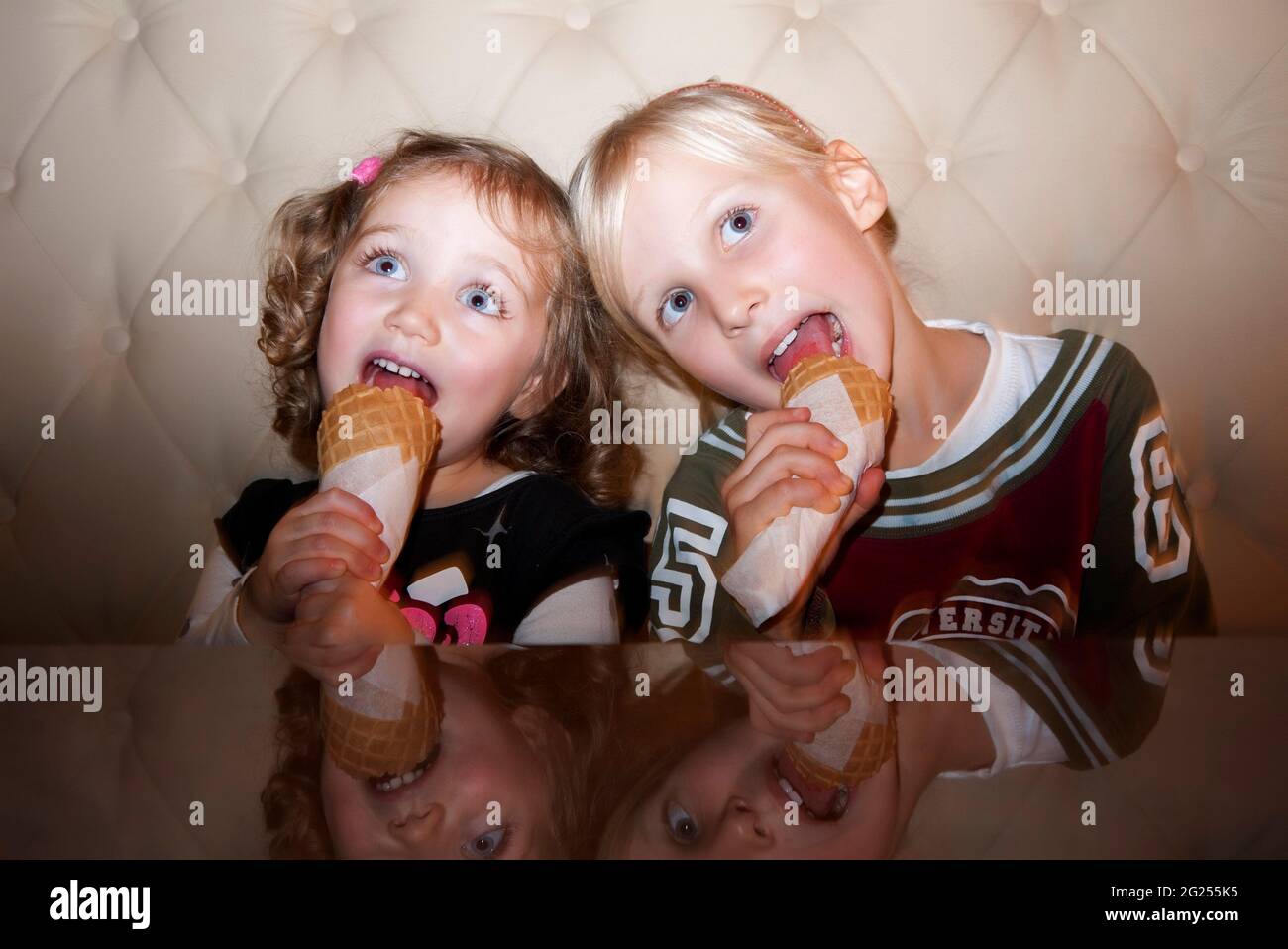 Zwei Mädchen sitzen auf einem Sofa und essen Eiszapfen Stockfoto