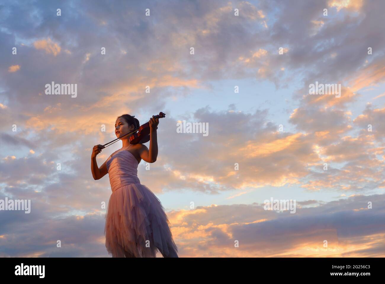 Frau, die bei Sonnenuntergang draußen steht und Geige spielt, Thailand Stockfoto