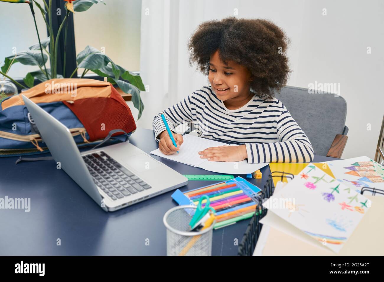 Fernunterricht, Online-Bildung für Kinder. Die kleine afroamerikanische Schülerin studiert zu Hause und macht ihre Schulaufgaben, sitzt an der Lasche Stockfoto