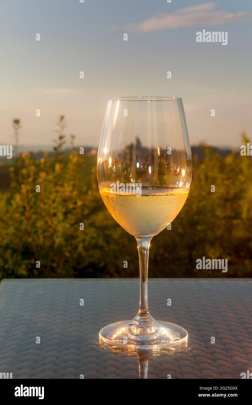 Glasse mit kaltem Weißwein während der Sonnenuntergangszeit auf Glas-Tabble mit Hügeln von Langhe, Italien, im Hintergrund Stockfoto