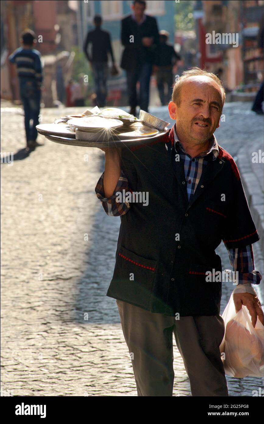 Ein Kellner im türkischen Restaurant, der ein Tablett mit Speisen zum Abendessen in einer gepflasterten Straße in Istanbul, Türkei, gebracht hat Stockfoto