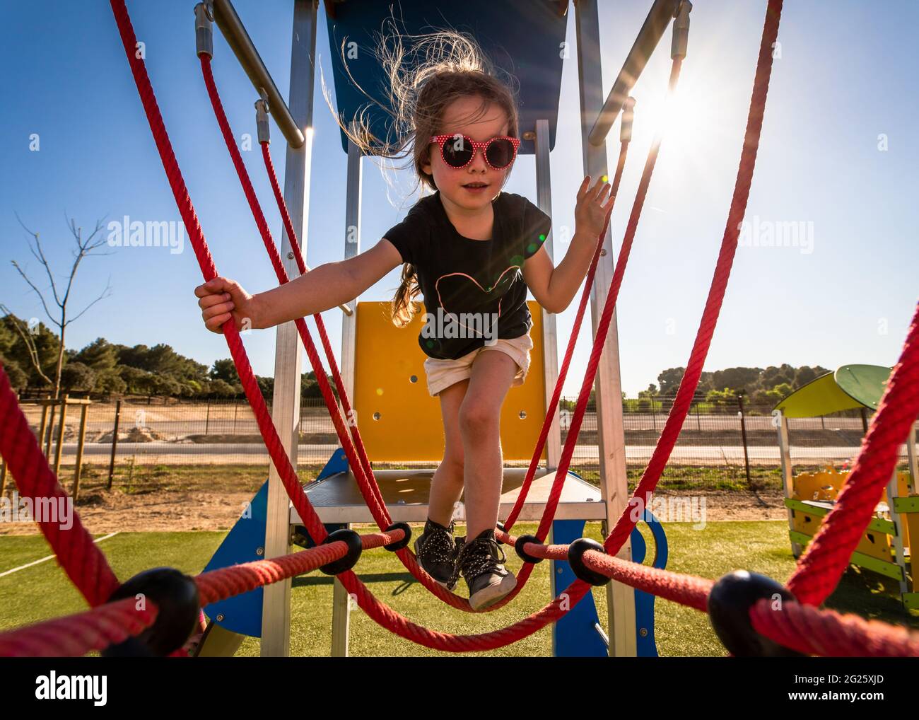 Junges Mädchen auf Klettergerüst im Outdoor-Park bei Sonnenschein Stockfoto