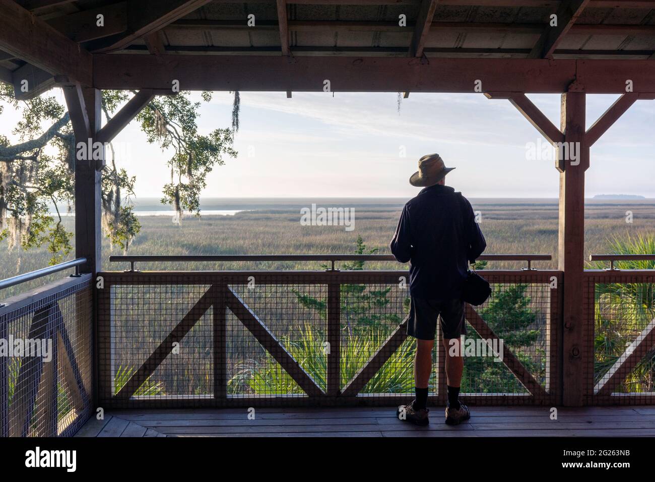 Ein älterer Mann auf einer großen Veranda nimmt den wunderschönen Landschaftshintergrund eines Tieflandsalzes in der Nähe von Sapelo Island, an der Küste von Georgia, USA, auf. Stockfoto