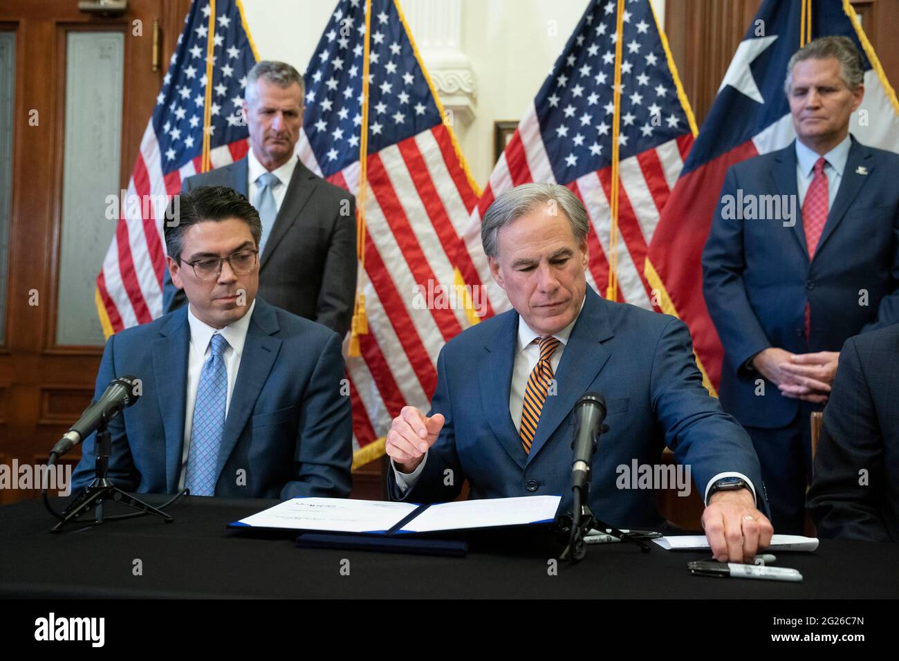 Austin, Texas USA, Juni 8 2021: Texas Gov. Greg Abbott greift nach einem Stift, um zwei Gesetzesvorlagen zur Stärkung des texanischen Stromnetzes und der Infrastruktur zu unterzeichnen, die auf seiner legislativen Tagesordnung standen. Die Rechnungen waren als Reaktion auf den Wintersturm im Februar, der Teile des texanischen Stromnetzes ausschlug und Millionen von Texanern während der Rekordtemperaturen tagelang ohne Strom auskam. Auf der linken Seite befindet sich der Rep. Chris Paddie, R-Marshall. Kredit: Bob Daemmrich/Alamy Live Nachrichten Stockfoto
