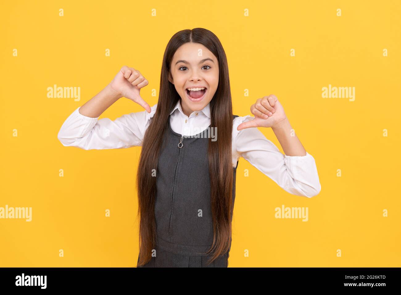 Glücklich Grundschule Mädchen Kind Lächeln zeigen Daumen Finger gelb Hintergrund, Bildung Stockfoto
