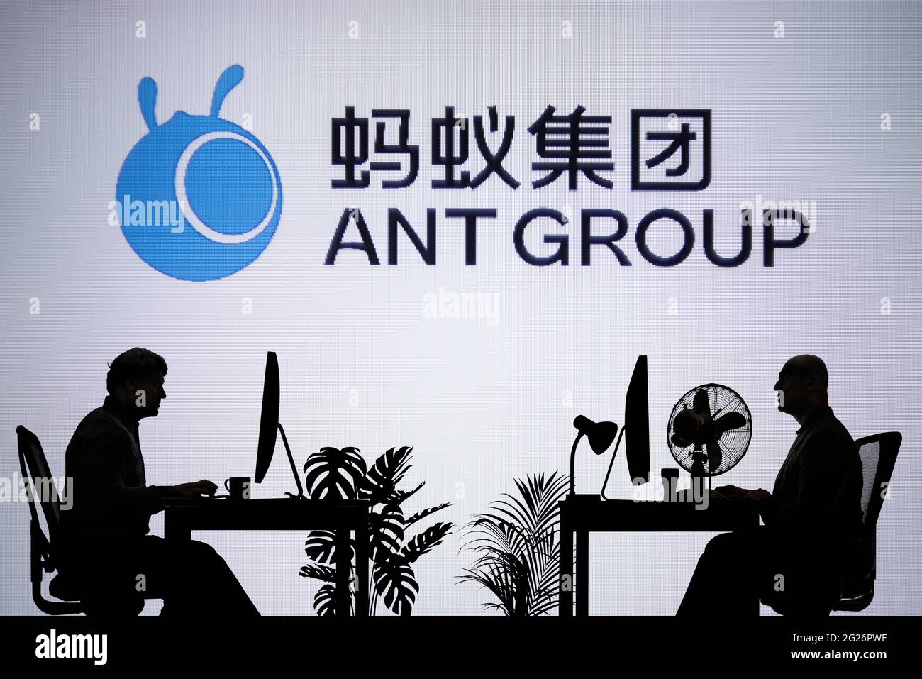 Das Logo der Ant Group ist auf einem LED-Bildschirm im Hintergrund zu sehen, während zwei silhouettierte Menschen in einer Büroumgebung arbeiten (nur zur redaktionellen Verwendung) Stockfoto