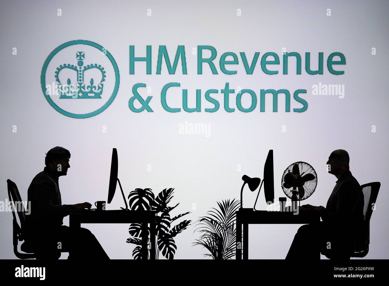 Das HMRC-Logo ist auf einem LED-Bildschirm im Hintergrund zu sehen, während zwei silhouettierte Personen in einer Büroumgebung arbeiten (nur zur redaktionellen Verwendung) Stockfoto