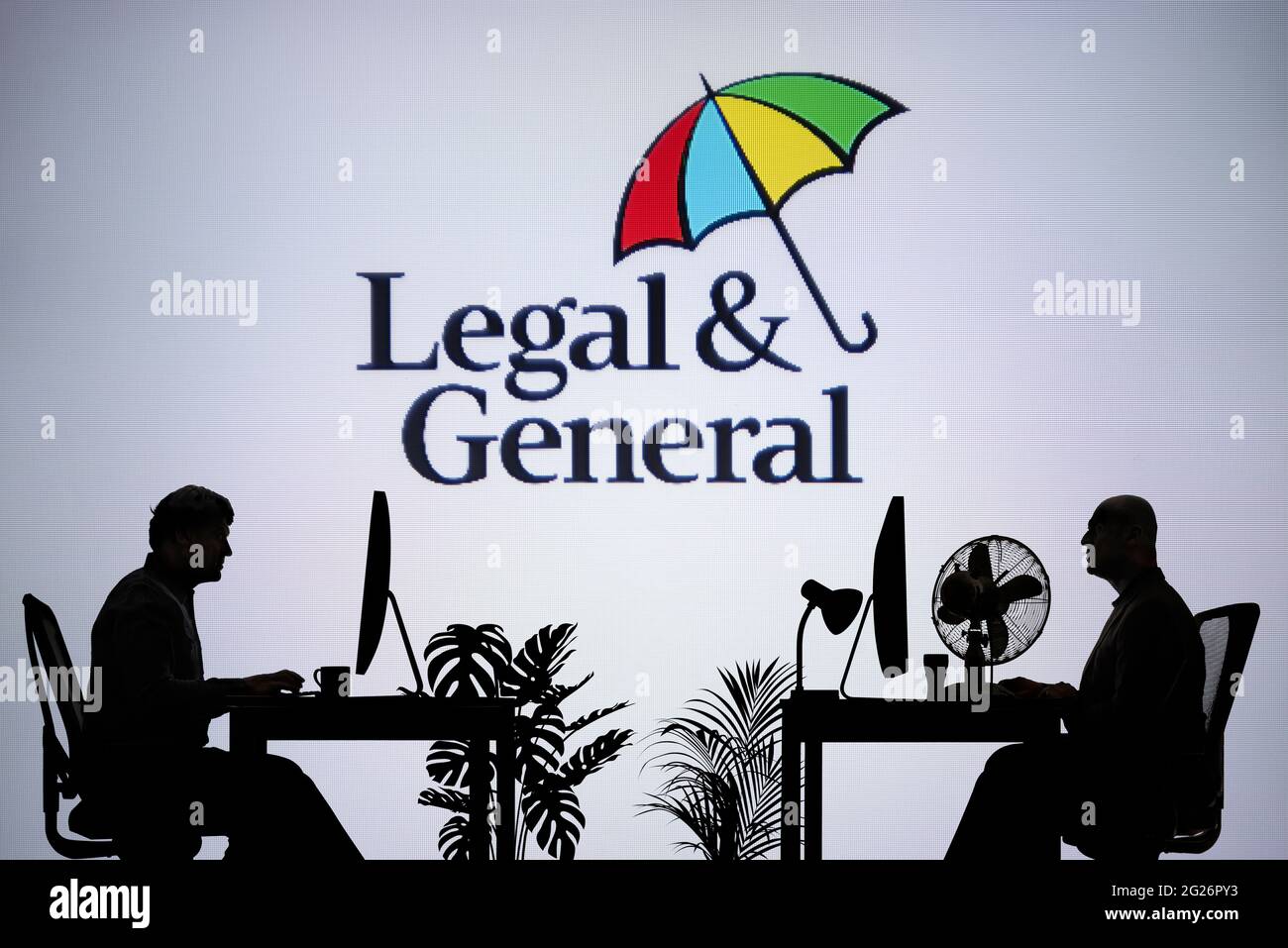 Das rechtliche und allgemeine Logo ist auf einem LED-Bildschirm im Hintergrund zu sehen, während zwei silhouettierte Personen in einer Büroumgebung arbeiten (nur zur redaktionellen Verwendung) Stockfoto