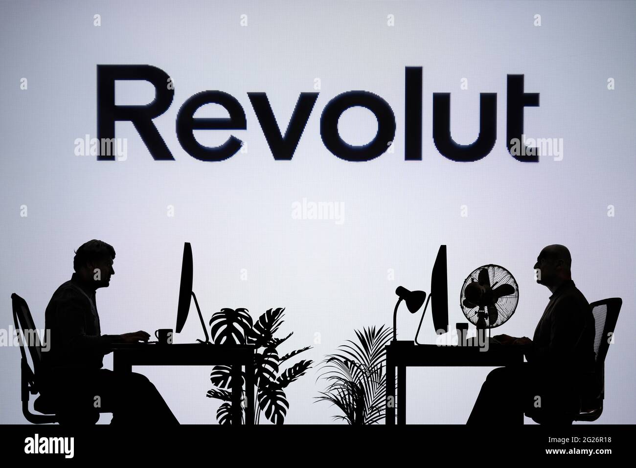 Das Revolut-Logo ist auf einem LED-Bildschirm im Hintergrund zu sehen, während zwei silhouettierte Menschen in einer Büroumgebung arbeiten (nur zur redaktionellen Verwendung) Stockfoto