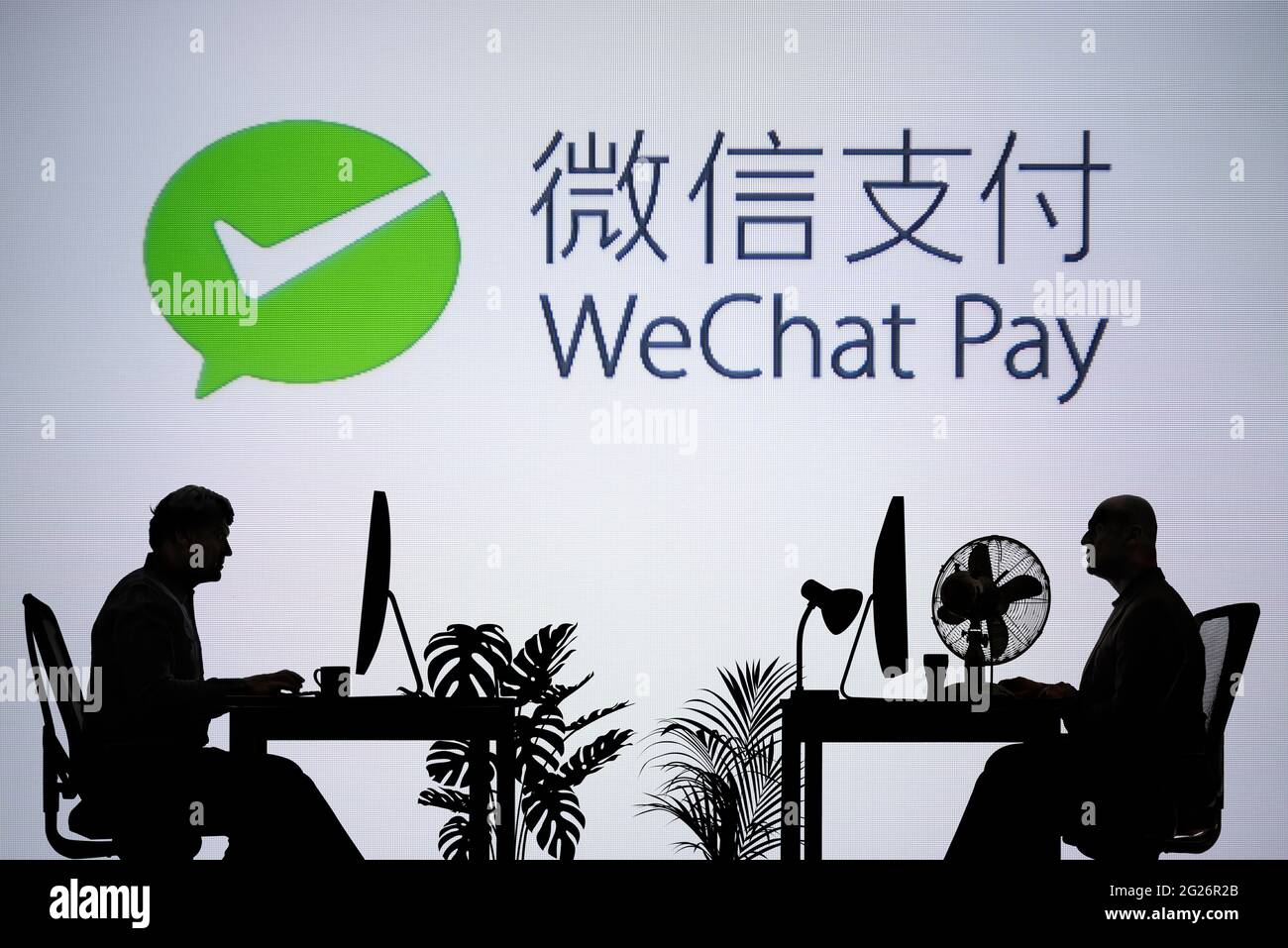 Das WeChat Pay-Logo ist auf einem LED-Bildschirm im Hintergrund zu sehen, während zwei silhouettierte Menschen in einer Büroumgebung arbeiten (nur zur redaktionellen Verwendung) Stockfoto