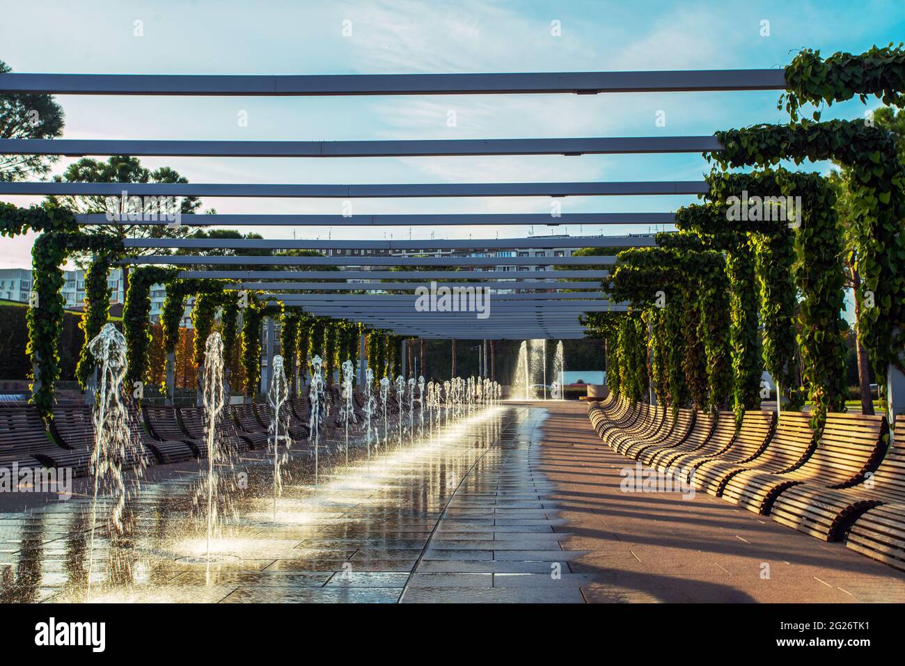 Erstaunliche Linie der kleinen Brunnen im Park Galitskogo in Krasnodar. Sonnenuntergang und Reihe von Holzbänken. Deutsches Projekt im Süden Russlands realisiert. Stockfoto