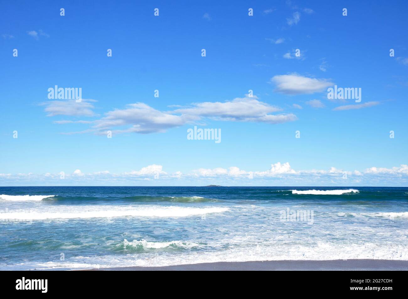 Kleine Wellen am Strand mit blauem Himmel und Wolken Stockfoto
