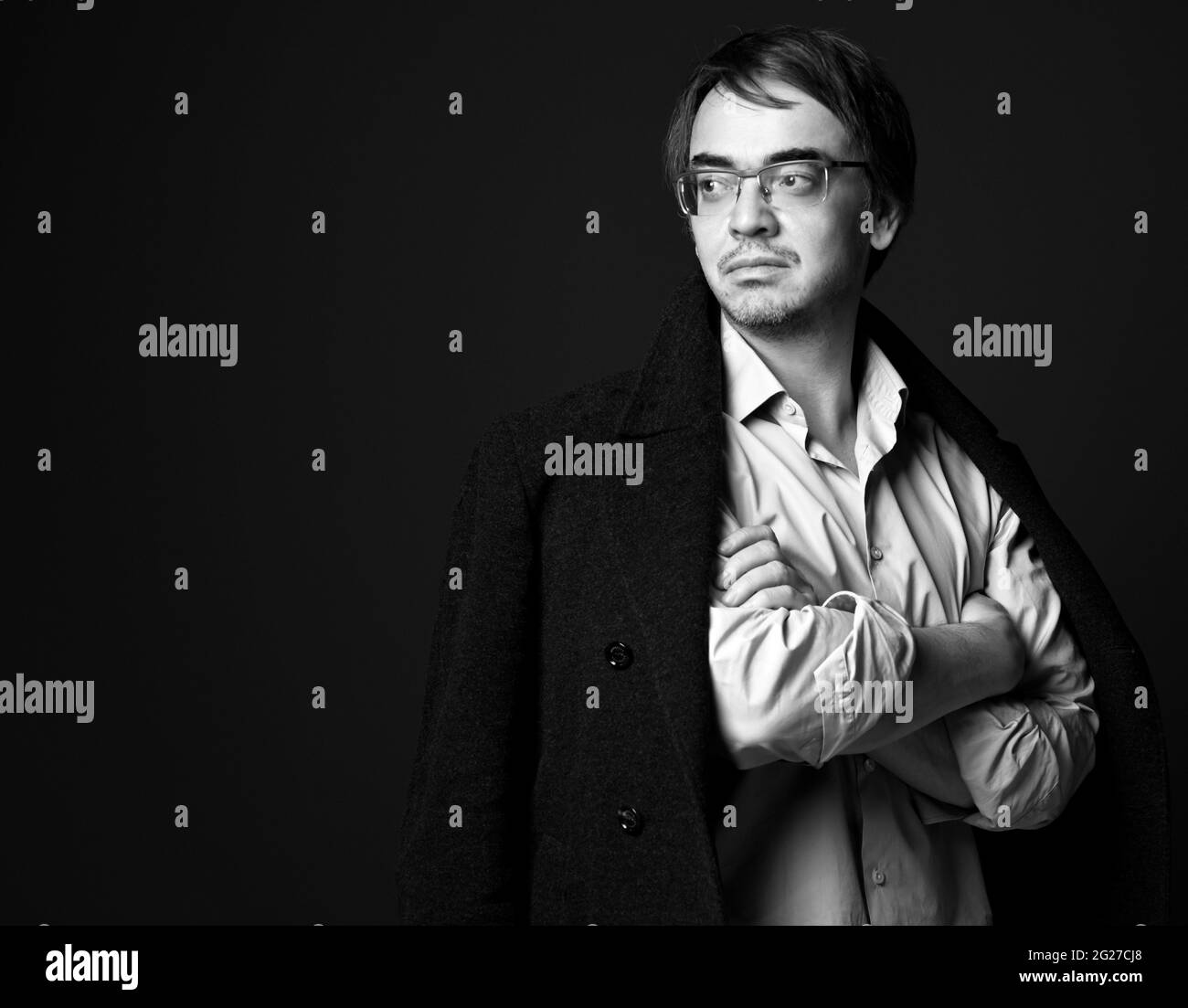 Schwarz und Weiß. Starker selbstbewusster erwachsener Mann in weißem Hemd und T-Shirt-Jacke auf Schultern stehend mit gekreuzten Armen Stockfoto