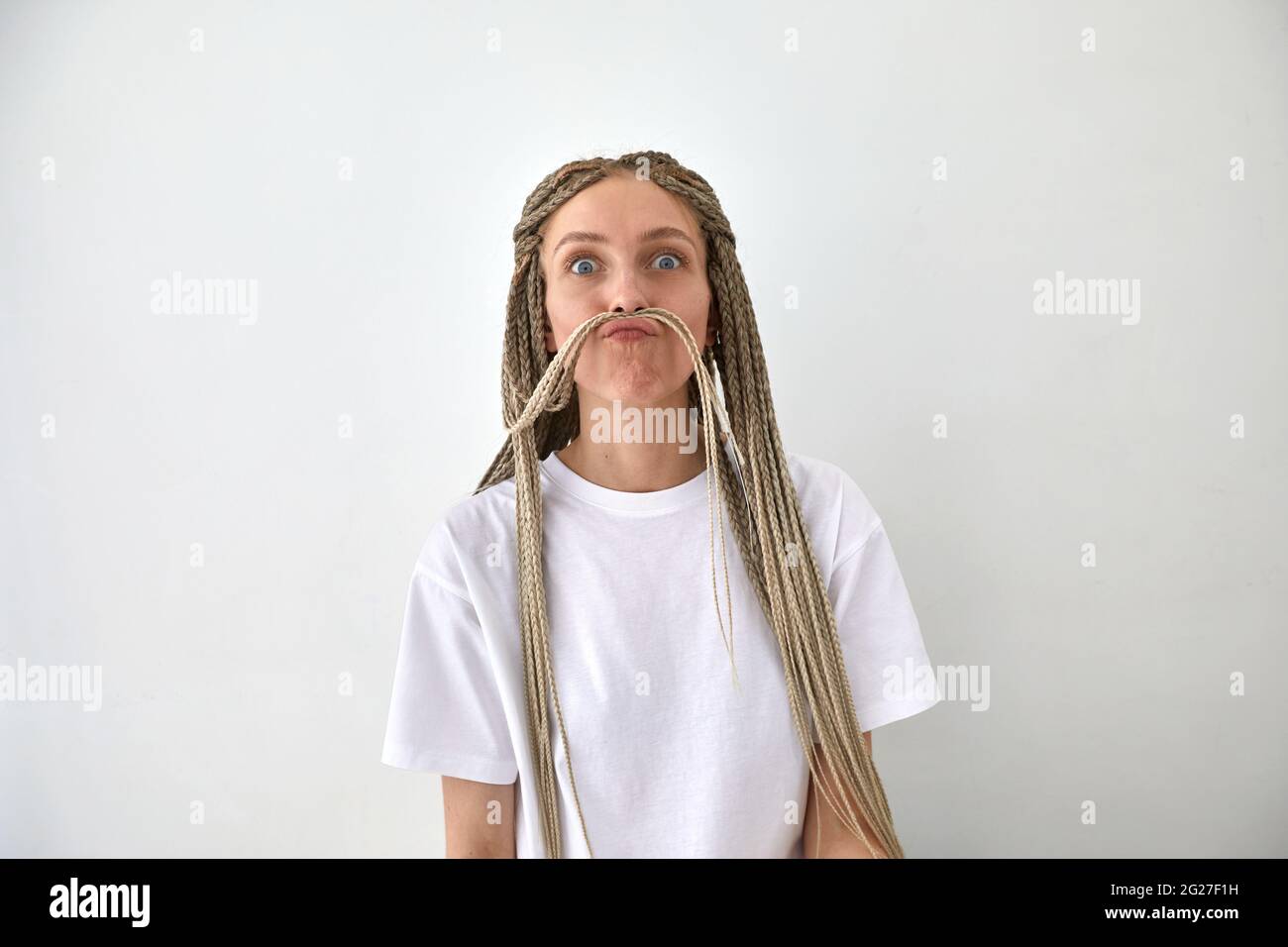 Weibchen mit langen geflochtenen Haaren, die die Lippen vor weißem Hintergrund verspielt und die Kamera anschaut Stockfoto