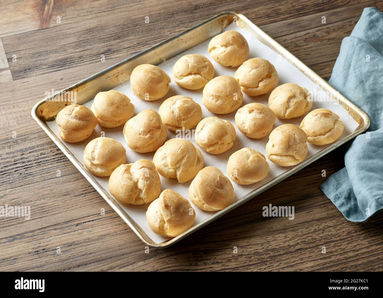 Frisch gebackene Cremepuffs auf der Backform auf dem hölzernen Küchentisch Stockfoto