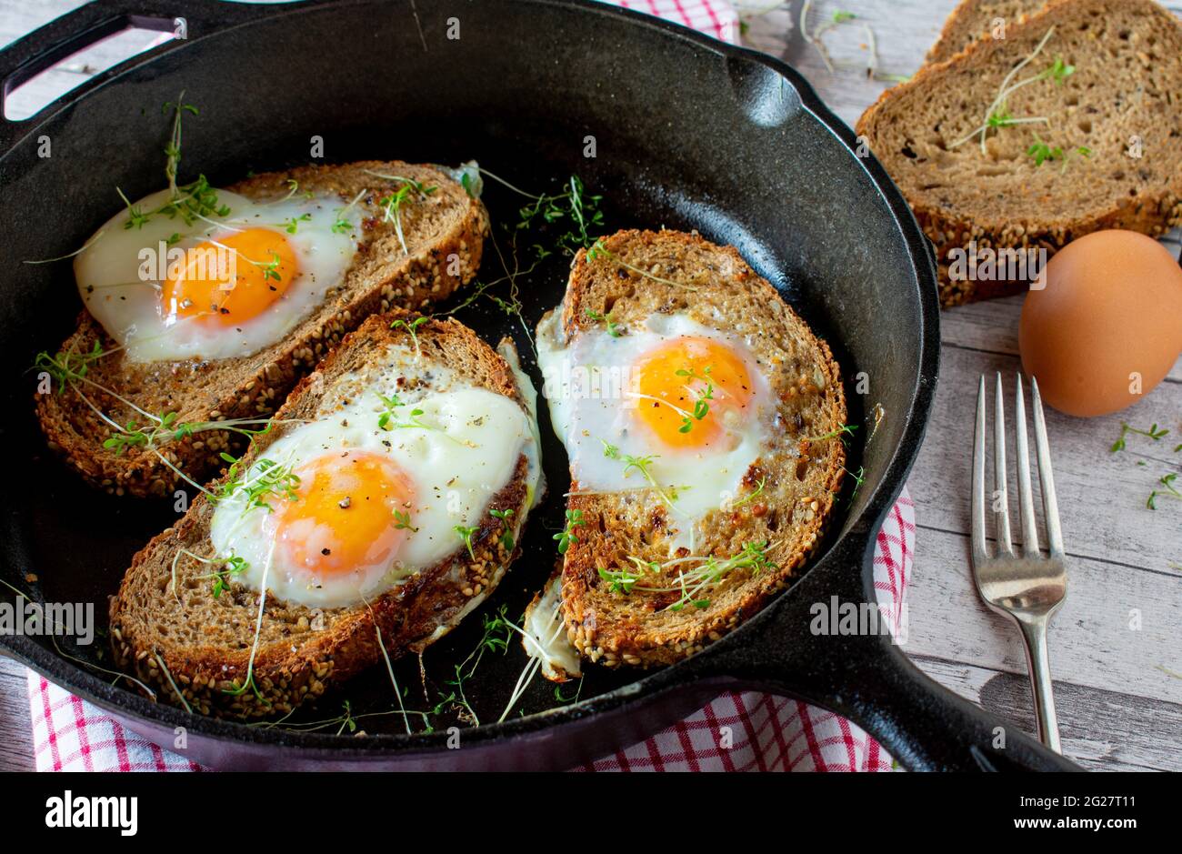 Ei im Ganzen serviert in gusseiserner Pfanne auf rustikalem und hölzernen Tischhintergrund Stockfoto