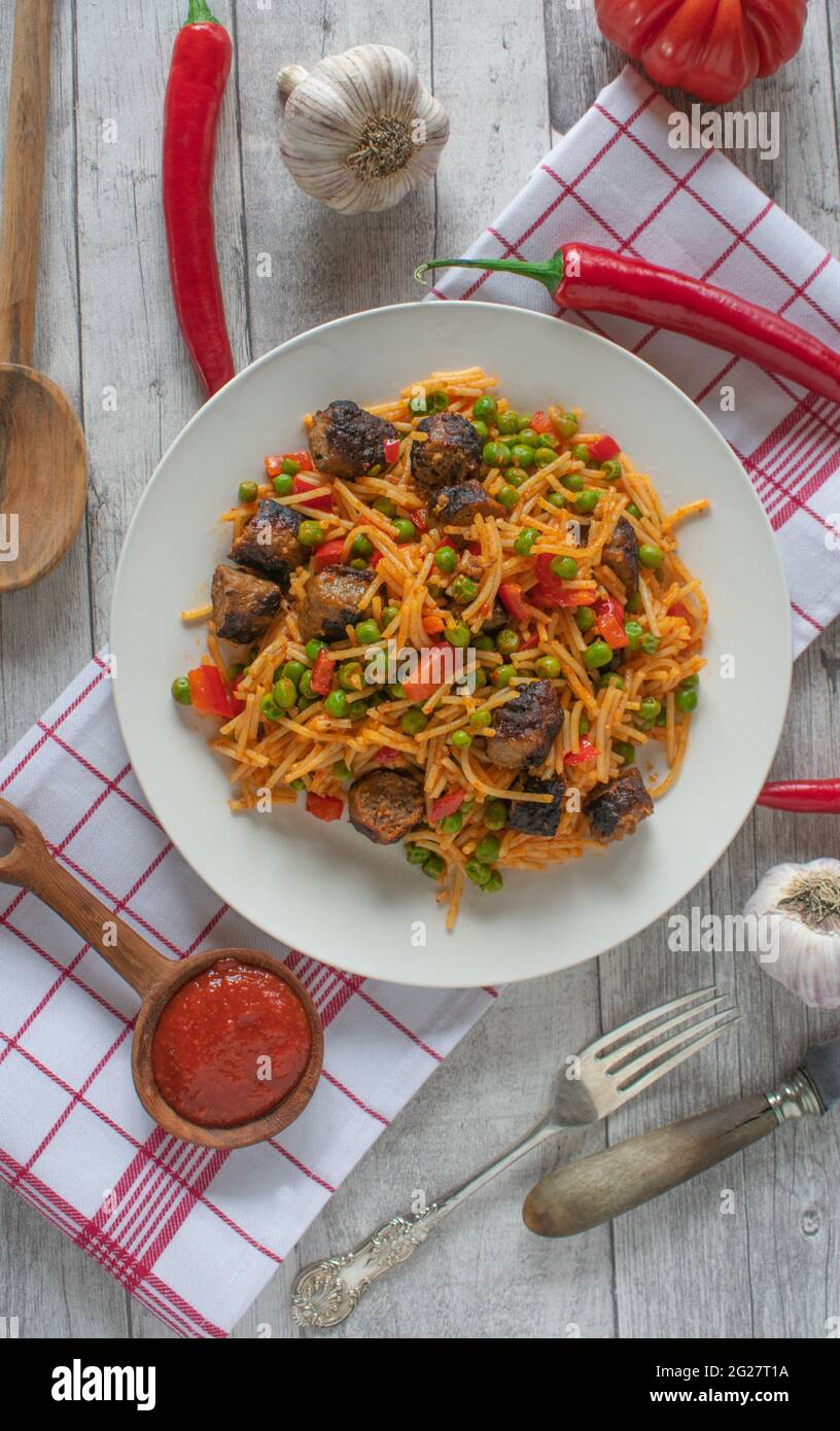 Glutenfreies Nudelgericht mit serbischen Cevapcici, Ajvar und Gemüse auf einem Teller Stockfoto