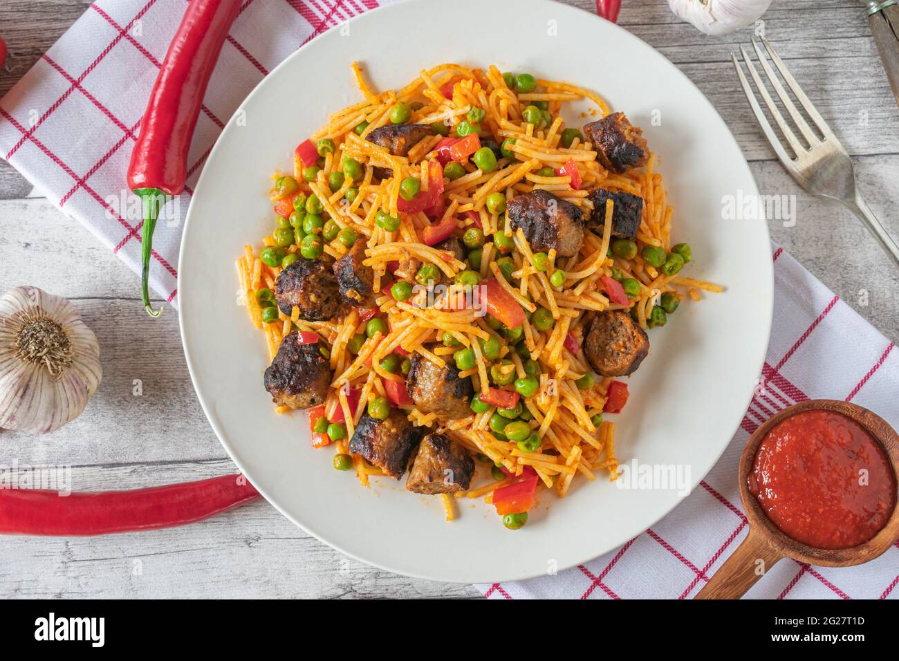 Glutenfreies Nudelgericht mit serbischen Cevapcici, Ajvar und Gemüse auf einem Teller Stockfoto