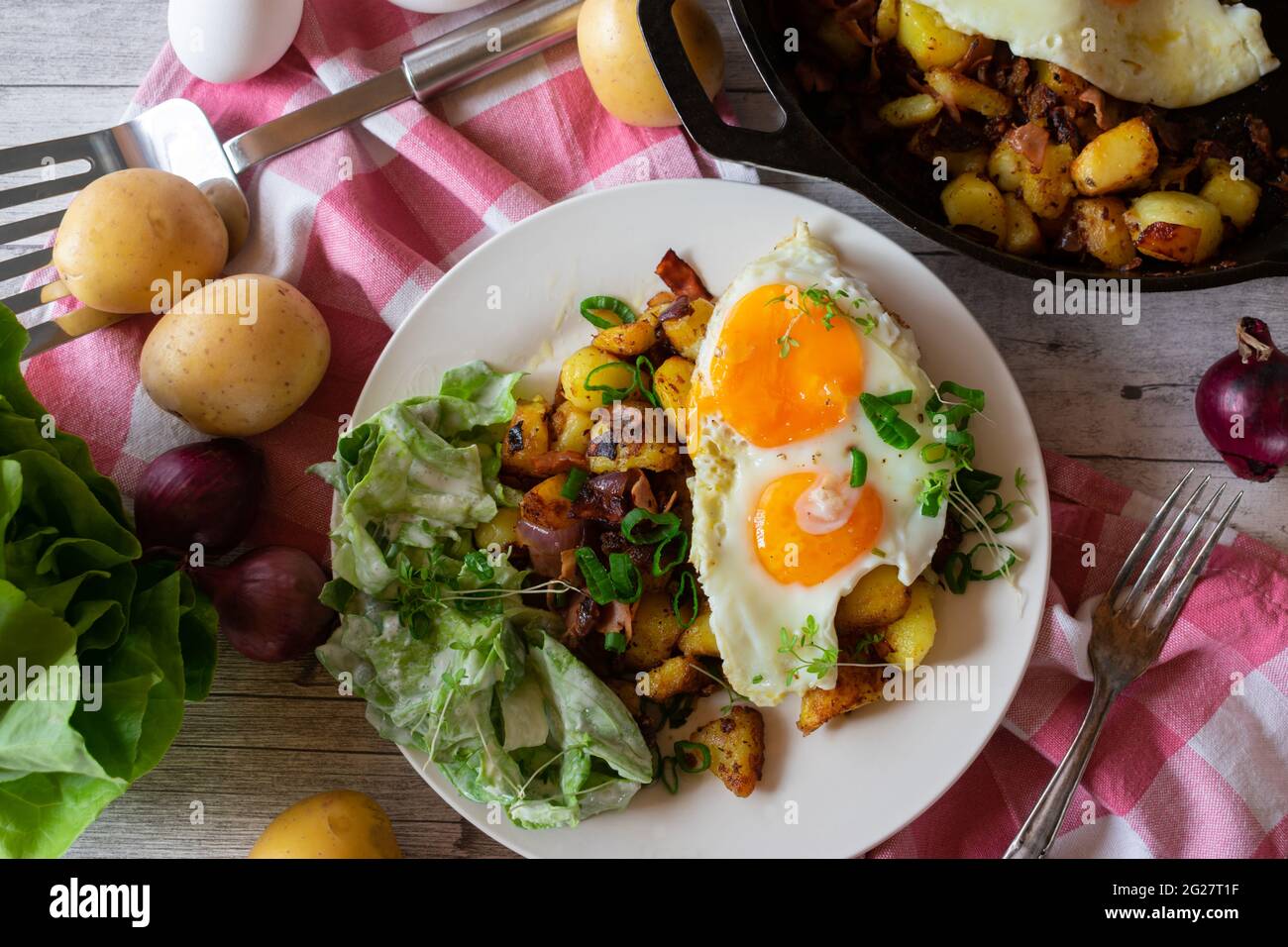 Herzhaftes vegetarisches Landgericht mit Bratkartoffeln, Eiern und Salat mit Sauerrahm-Dressing, serviert auf einem Teller auf rustikalem Holztisch-Hintergrund Stockfoto