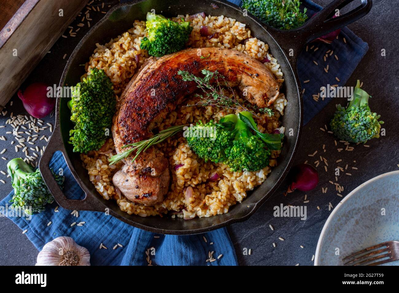 Gesunde Ernährung fettarmes Fitnessmenü mit Schweinebraten, braunem Reis und Brokkoli, serviert in einer rustikalen gusseisernen Pfanne von oben. Stockfoto
