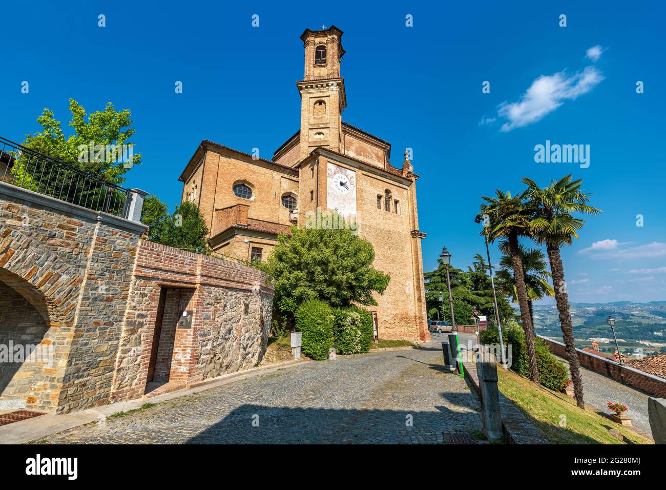 Enge gepflasterte Straße und alte Backsteinkirche unter blauem Himmel in der Kleinstadt Guarene im Piemont, Norditalien. Stockfoto