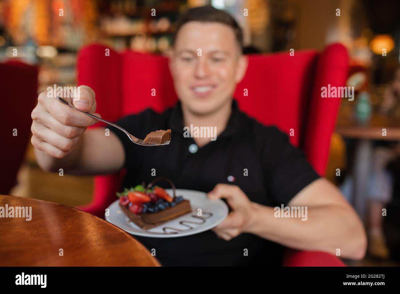 Ein disfokussierter Mann hält ein Stück Schokoladendessert auf einem Löffel vor die Kamera Stockfoto