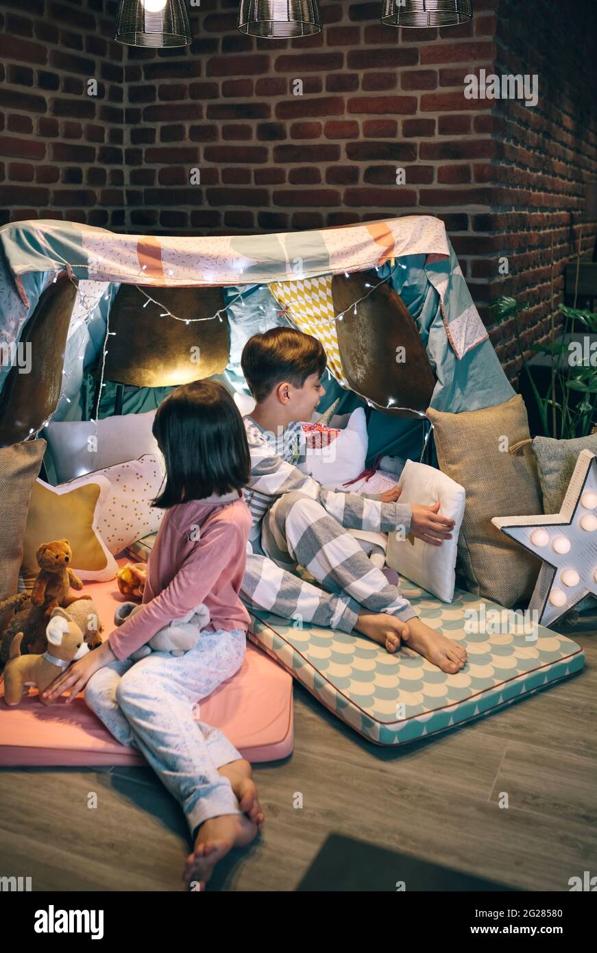 Kinder bereiten Zelt mit Stühlen und Bettwäsche für eine Pyjama-Party vor Stockfoto