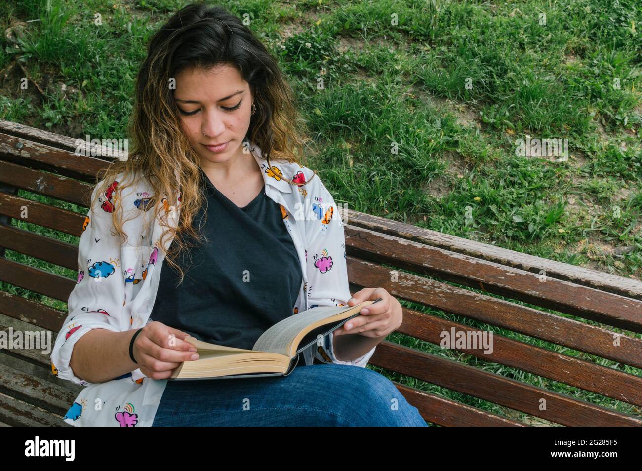 Hübsches junges Mädchen, das ein Buch auf einer Bank in einem Park liest Stockfoto