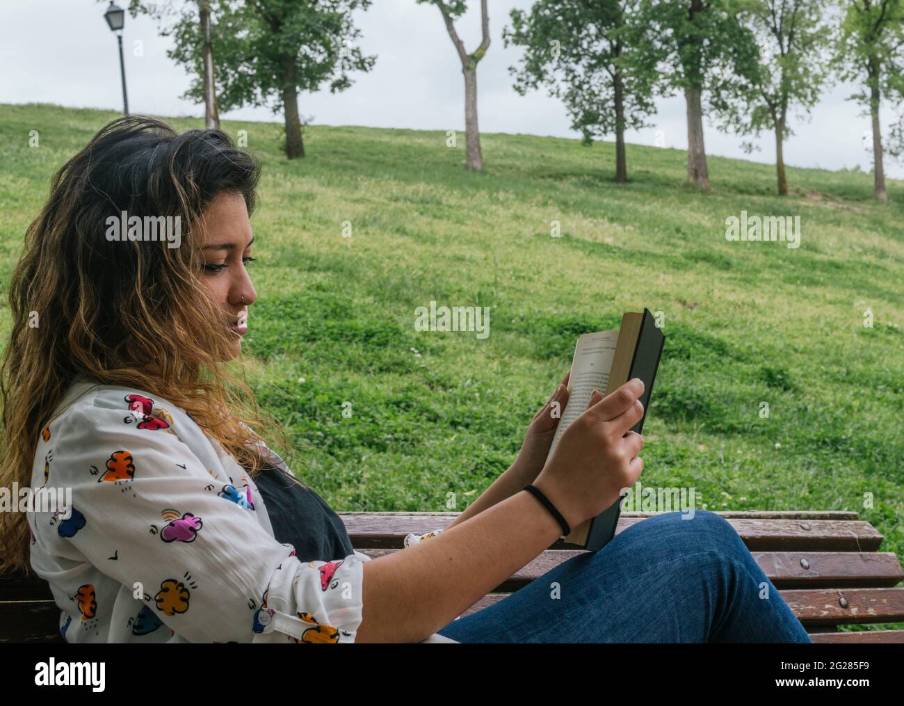 Hübsches junges Mädchen, das ein Buch auf einer Bank in einem Park liest Stockfoto