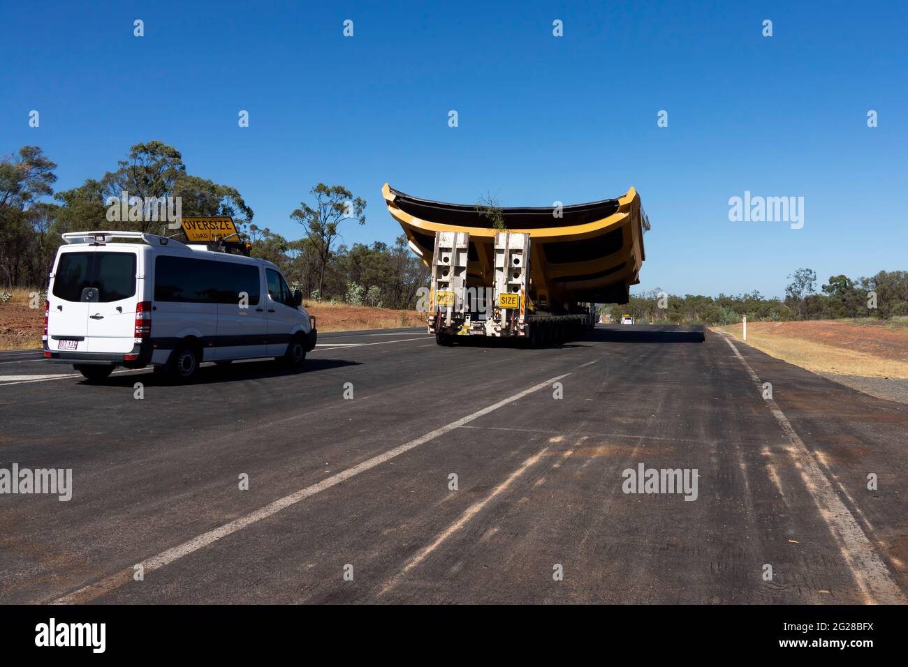 Eine Rückansicht eines großen LKWs, der ein Tablett für einen Monster Mining Dump Truck mit seiner Begleitung von Pilotfahrzeugen transportiert, die eine Warnung mit Kopieplatz geben. Stockfoto