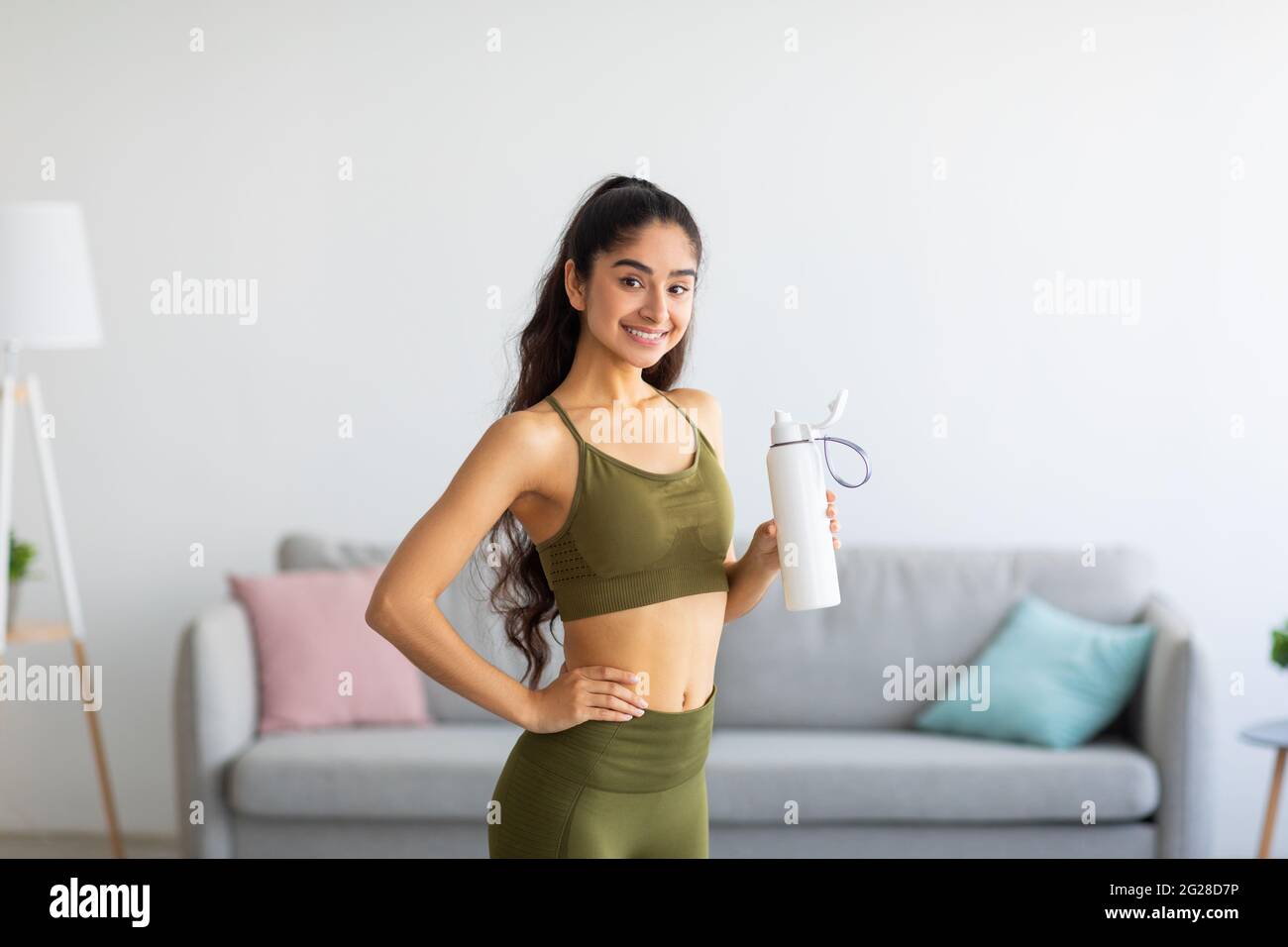 Millennial Indian Frau in Sportkleidung Trinkwasser oder Protein-Shake aus der Flasche zu Hause Stockfoto