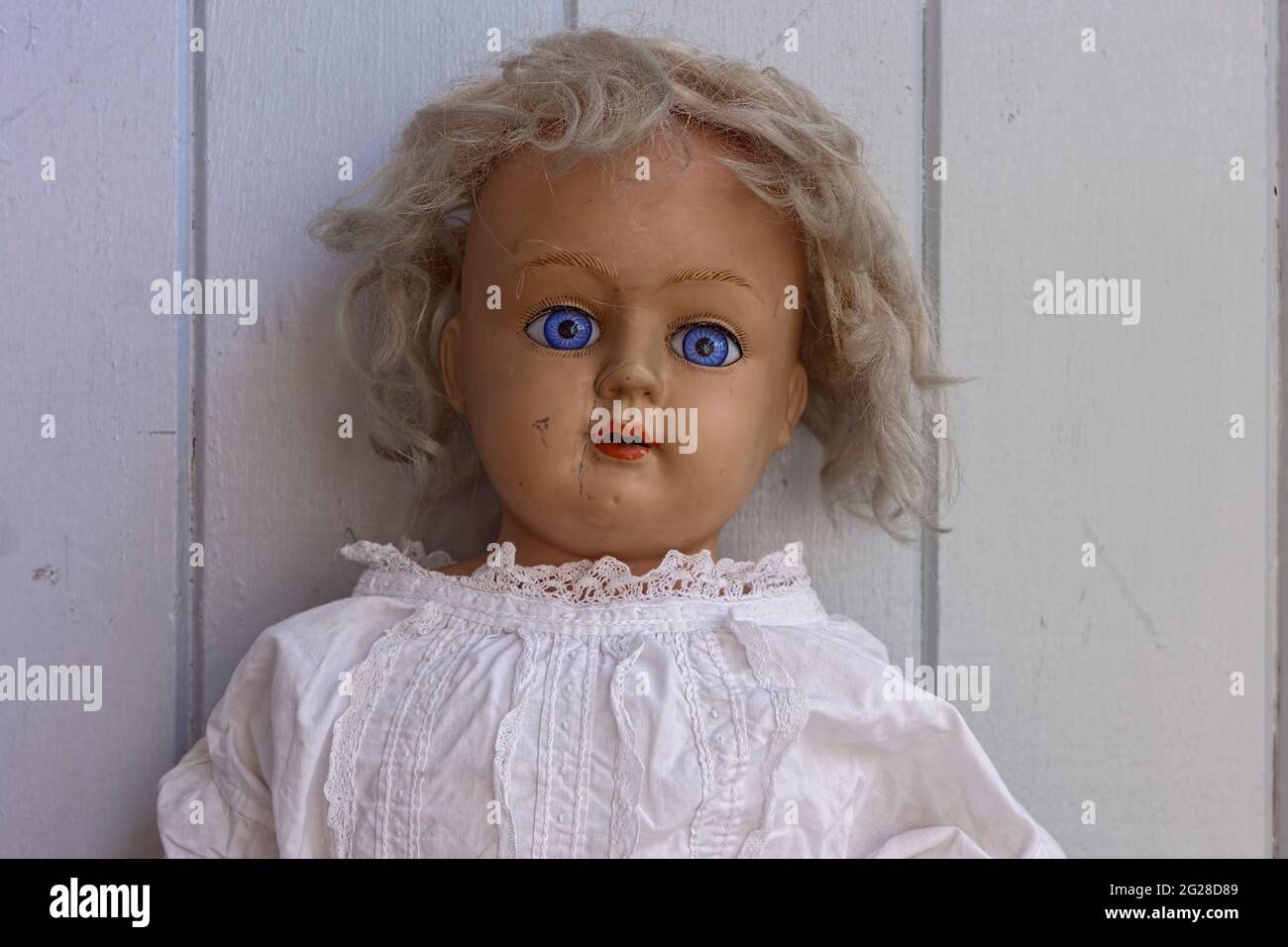 Gruselige, gruselige alte antike Puppe mit starrenden blauen Augen und Narbe und mit unordentlichen blonden Haaren für halloween Stockfoto