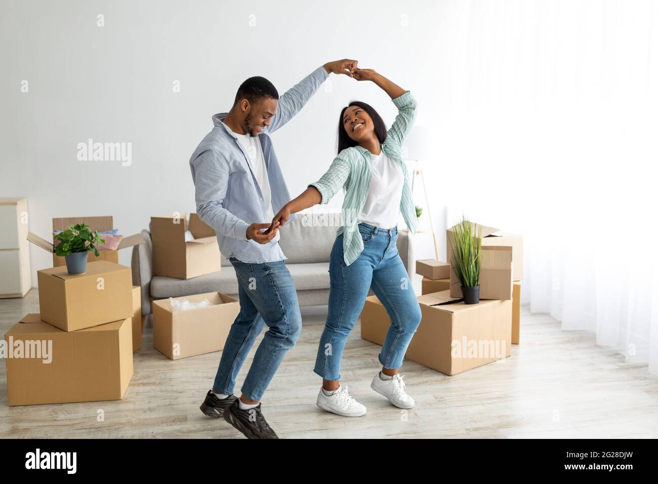 Fröhliche, liebevolle schwarze Ehepartner tanzen in ihrer neuen Wohnung zwischen Pappkartons am Umzugstag, freier Platz Stockfoto