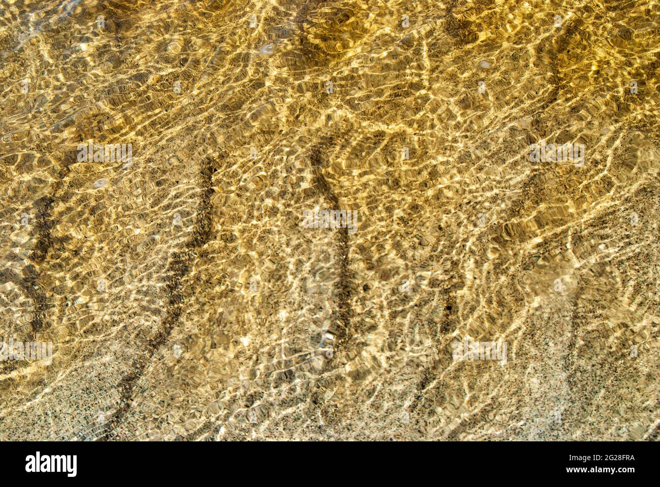 Reflexionen und Sandmuster im goldklaren Wasser eines kleinen Baches an der Küste der Insel Barra in den Äußeren Hebriden Schottlands. Stockfoto