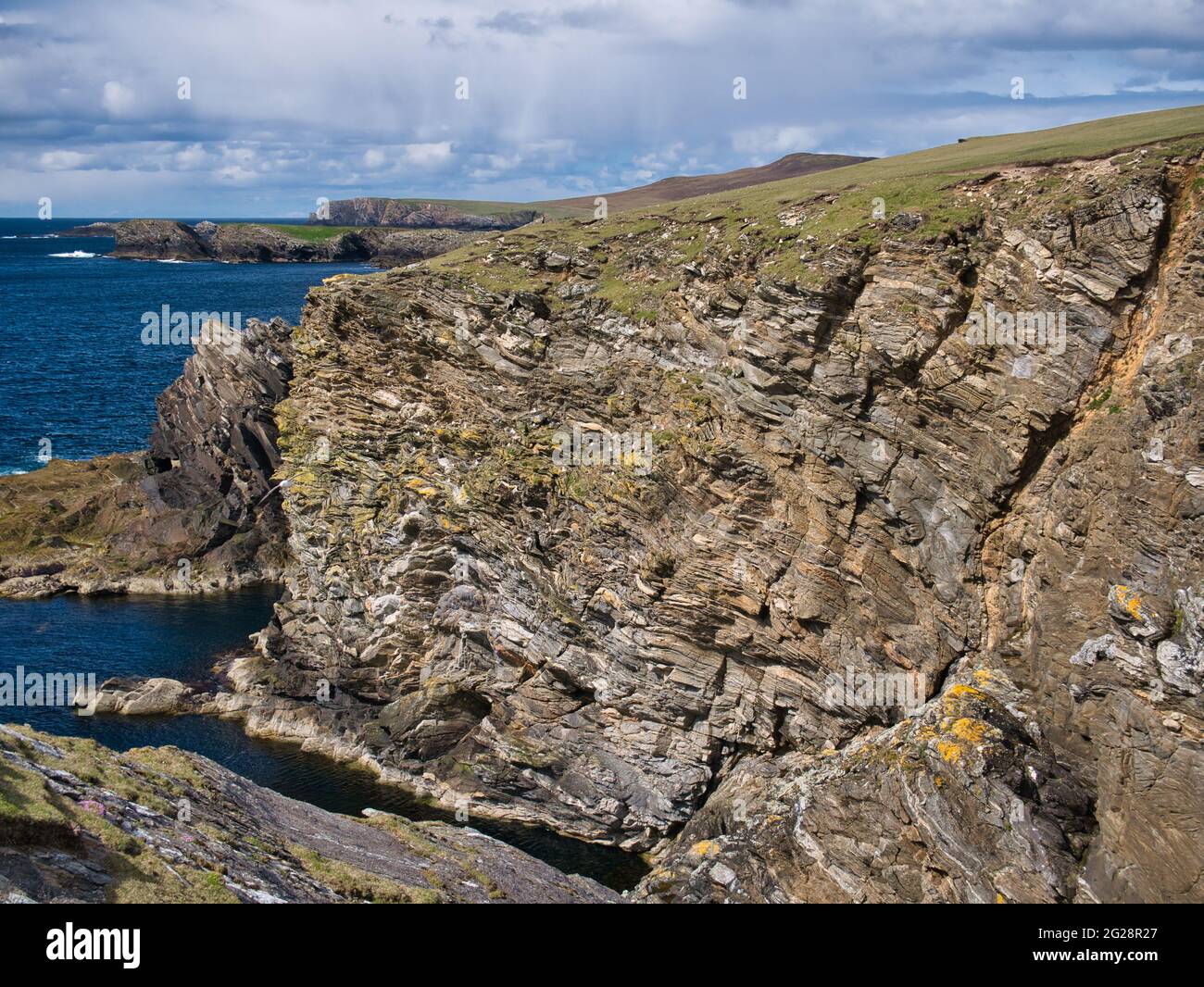 Küstenklippen rund um Collaster an der Westküste der Insel Unst, Shetland, Großbritannien. Die Gesteine sind erodiert, stark geschichtet und geneigt. Stockfoto
