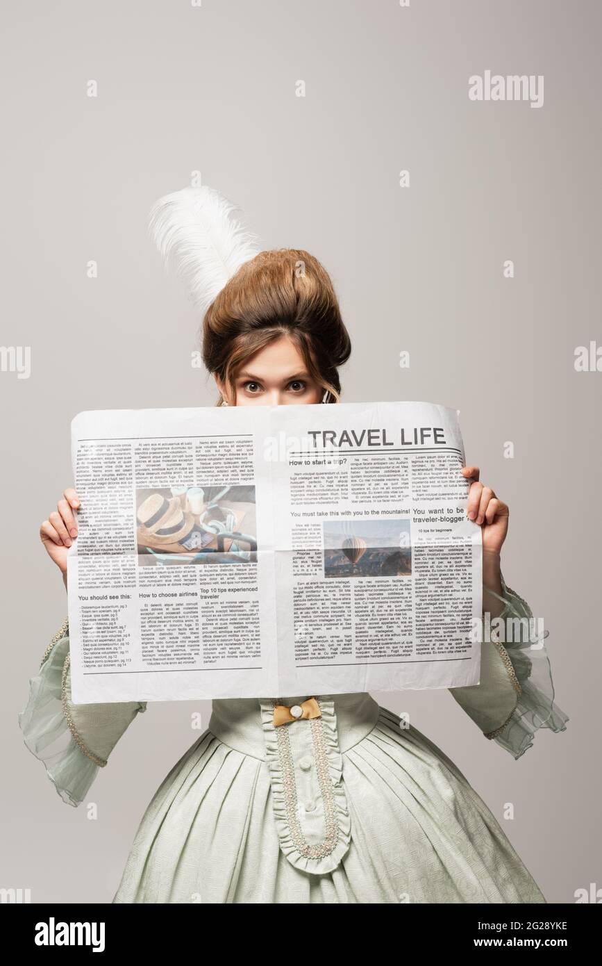 Frau im Retro-Stil verdunkelt das Gesicht mit einer Zeitung aus dem Reiseleben, die auf Grau isoliert ist Stockfoto