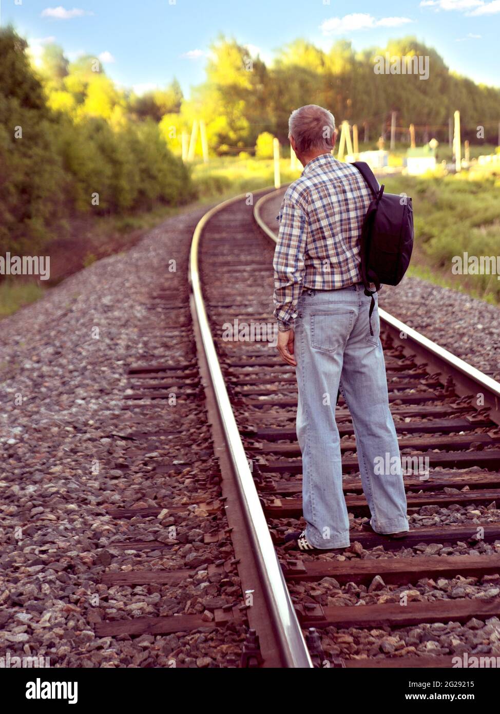 Älterer Mann in karierten Hemden und Denim-Hosen mit schwarzem Rucksack  steht auf Schienen der Eisenbahnstrecke Stockfotografie - Alamy