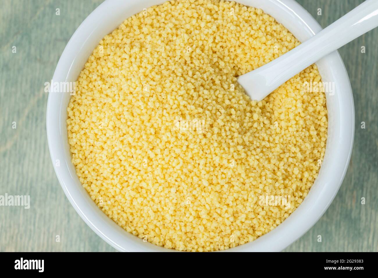 Couscous in weißer Palte. Schließen Sie gelben Couscous auf einem grünen Teller mit Löffel. Flach liegend. Draufsicht Stockfoto