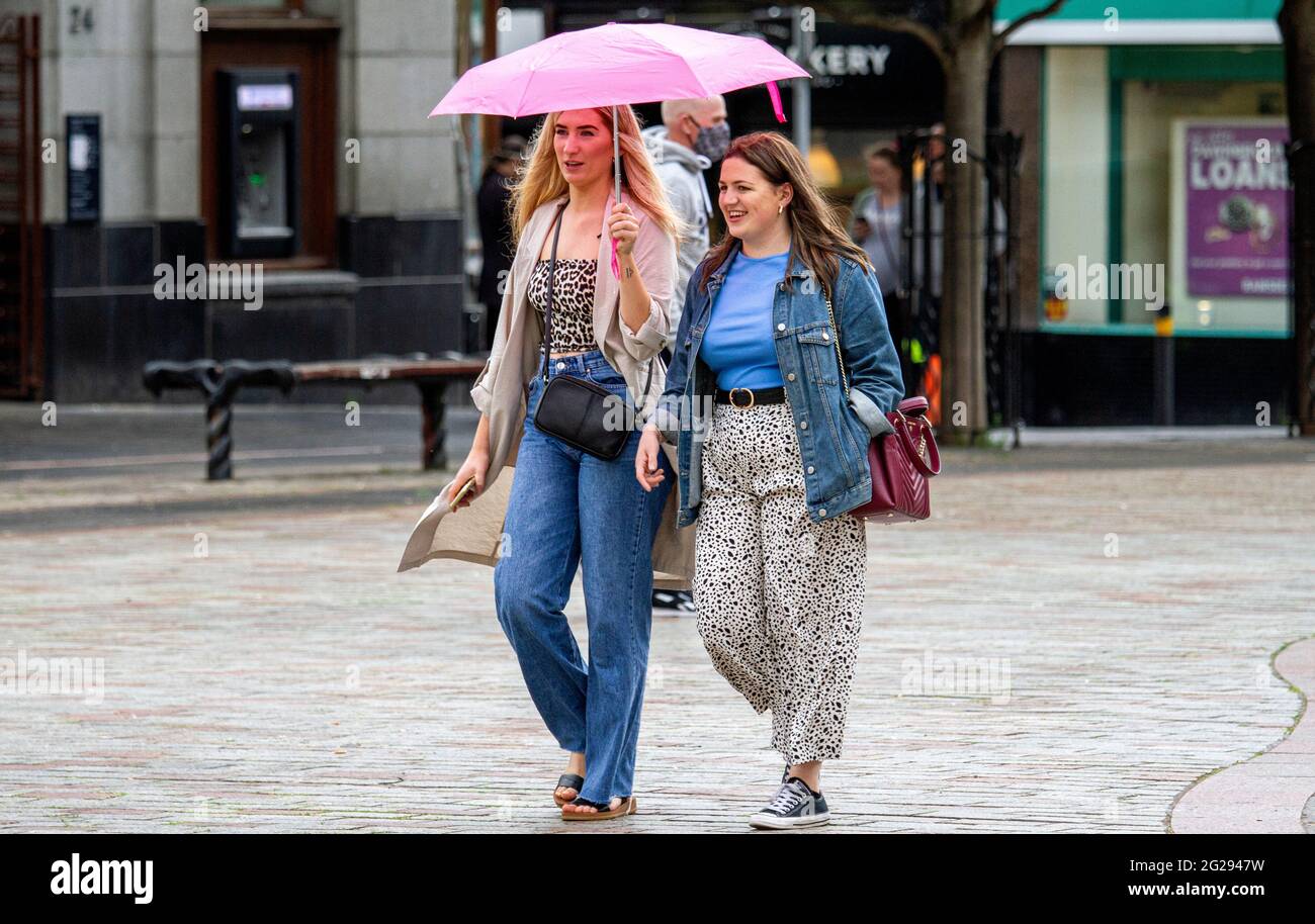 Dundee, Tayside, Schottland, Großbritannien. Juni 2021. UK Wetter: Ein bewölktes und feuchtes Wetter mit gelegentlichen leichten Schauern über Nordostschottland mit Temperaturen bis zu 20 Grad Covid-19 Lockdown-Beschränkungen haben sich in Dundee gelockert, da sich die Menschen immer noch der sozialen Distanzierungsrichtlinien und des Tragens von Gesichtsmasken bewusst sind. Zwei modische junge Frauen nehmen den Tag draußen und genießen ihre Freiheit beim gemeinsamen Gehen, während sie sich vor dem Regen unter einem Brüllchen im Stadtzentrum schützen. Kredit: Dundee Photographics/Alamy Live Nachrichten Stockfoto