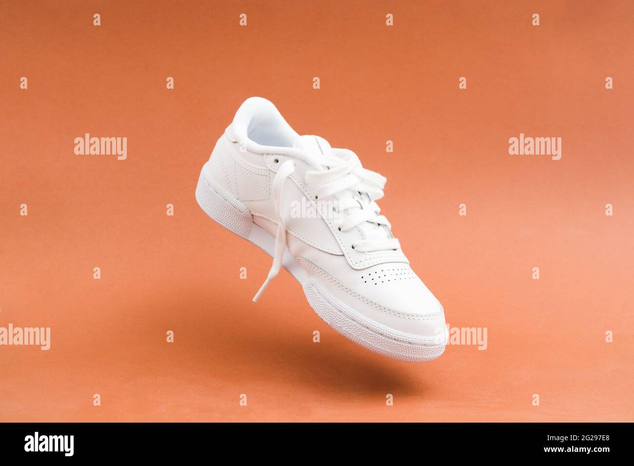 Levitation von einzelnen weiblichen stilvollen weißen lässigen Sneaker auf braunem Hintergrund Stockfoto