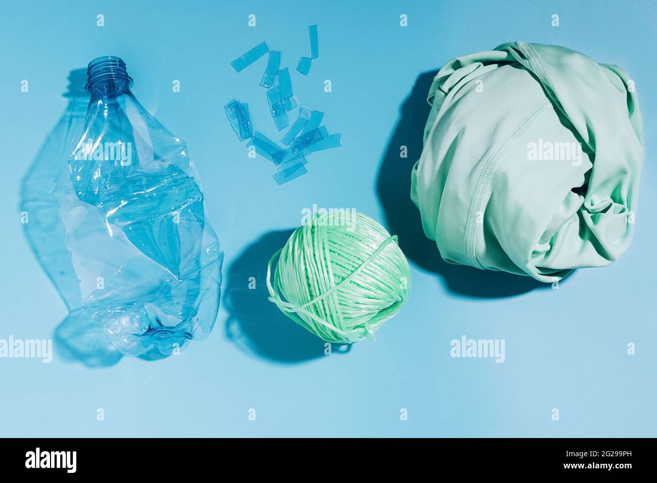 Das Konzept des Recyclings und der Wiederverwendung von Kunststoff. Leere Plastikflasche und recycelte Polyesterfaser, Synthetikgewebe auf blauem Hintergrund. Umwelt Stockfoto
