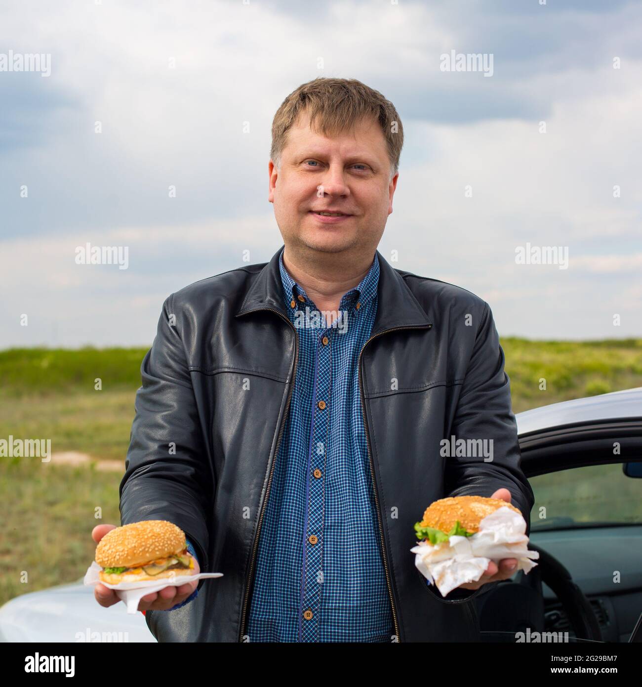 Ein Mann an der frischen Luft behandelt Hamburger, die seine Hände aushalten. Stockfoto