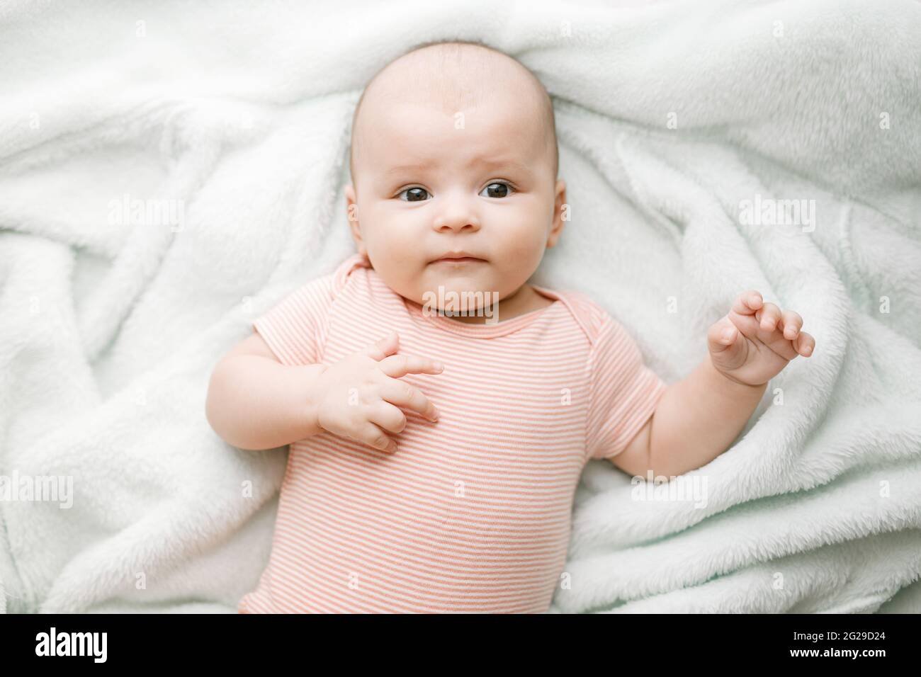 Entzückendes Baby im sonnigen Schlafzimmer. Das neugeborene Baby ruht in einer warmen, weichen Bettdecke. Lächelndes Kind, das die Kamera anschaut. Stockfoto