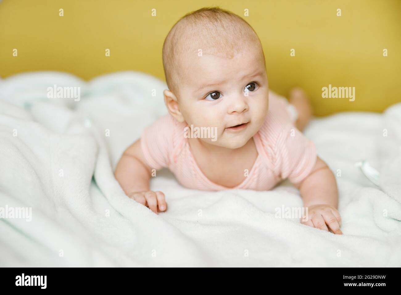 Entzückendes Baby im sonnigen Schlafzimmer. Das neugeborene Baby ruht in einer warmen, weichen Bettdecke. Lächelndes Kind, das die Kamera anschaut. Stockfoto
