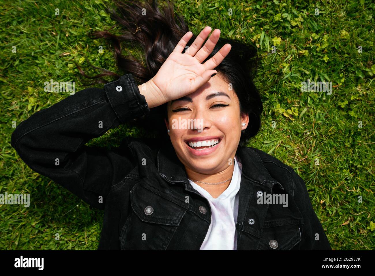 Overhead einer jungen lateinischen Frau, die auf dem Gras liegt und Spaß hat Stockfoto