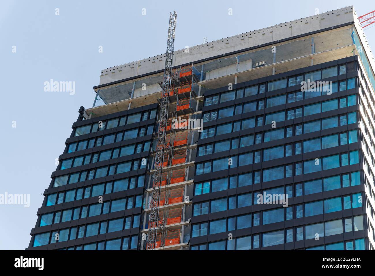 basel schweiz april 24. 2021: Blauer Wolkenkratzer mit roter Konstruktion und Gerüstaufzug vor wolkenlosem Himmel, in großen Städten immer mehr const Stockfoto