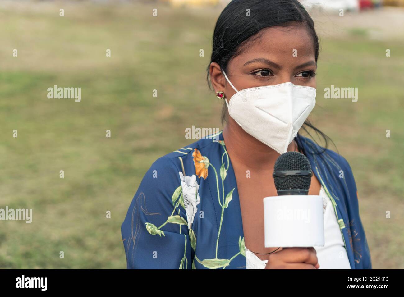 Reporterin trägt Maske und spricht über das Mikrofon, während sie auf steht Straße in der Stadt Stockfoto