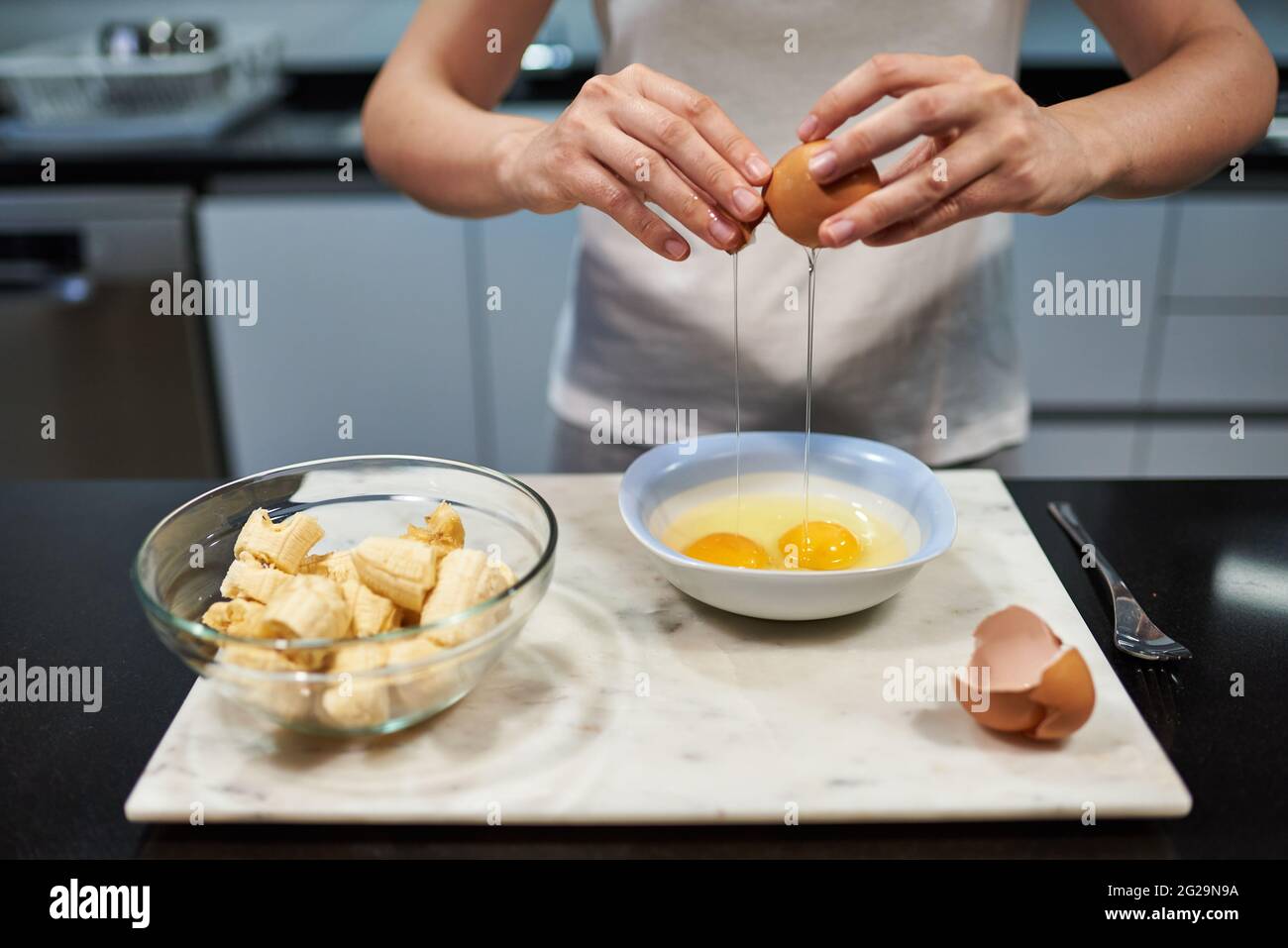 Frau öffnet ein Ei für einen Bananenpfannkuchen Rezept Stockfoto