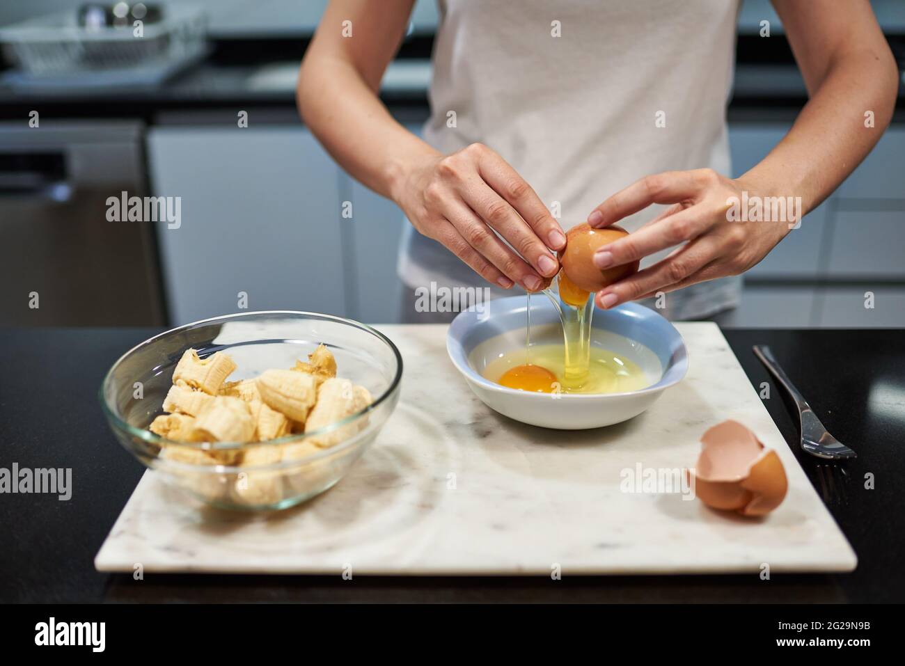 Frau öffnet ein Ei für einen Bananenpfannkuchen Rezept Stockfoto